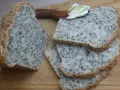 Chleb na proszku do pieczenia, bogaty w ziarna, pokrojony na kromki. Na jednej z nich leży masło na drewnianej łopatce.