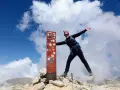 Donna esulta in cima al Monte Amaro dopo un trekking. Cielo azzurro e nuvole bianche.