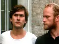 Dwóch mężczyzn na tle ceglanej ściany. Jeden w białej koszulce, drugi w czarnej. To fragment z filmu "Karate po polsku obsada".