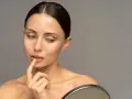 Mujer se toca los labios con el dedo, reflexionando sobre cómo hidratar los labios para una piel radiante.