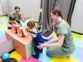 Dwie małe dziewczynki bawią się interaktywną kostką, a fizjoterapeutka wspiera jedną z nich. To może być część terapii wwr co to.