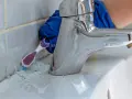 Main tenant utilise une brosse à dents pour nettoyer joint salle de bain.