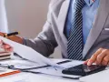 Radca skarbowy analizuje dokumenty i korzysta z kalkulatora, pracując nad finansami.