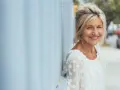 Donna sorridente appoggiata a un muro blu. Potrebbe beneficiare di acido folico in menopausa per il suo benessere.