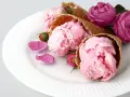 Drei Eiswaffeln mit rosa rosen eis, garniert mit Rosenblättern und Knospen auf einem weißen Teller.