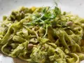 Makaron tagliatelle z zielonym sosem pesto, posypany pistacjami i udekorowany kiełkami.