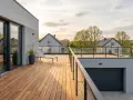 Nowoczesny garaż z tarasem na dachu, idealnym miejscem na relaks. Drewniany taras z leżakiem i szklanymi balustradami.