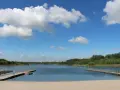 Piękny dzień nad jeziorem Wilczyńskim. Piaszczysta plaża, drewniane pomosty i błękitne niebo z białymi chmurami zapraszają do wypoczynku.