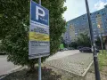 Płatny parking dla klientów Biedronki. Obok drzewa stoi znak informujący o cenniku i zasadach parkowania.