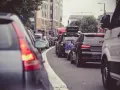 Korek w mieście, gdzie jest ruch lewostronny. Samochody stoją w rzędzie, widać znaki drogowe i budynki.