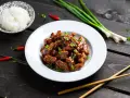 Pyszny kurczak luc lac w sosie, posypany szczypiorkiem i sezamem, obok miseczka ryżu, pałeczki i papryczki chili.