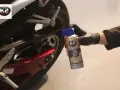 Ręka w czarnej rękawiczce aplikuje suchy smar do łańcucha motocyklowego K2. Idealny wybór, by zadbać o napęd.