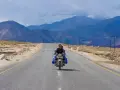 Mężczyzna na motocyklu przemierza pustynny krajobraz w Leh, Indie, z majestatycznymi górami w tle.