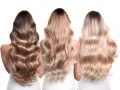 Trzy kobiety z falującymi włosami. Jedna ma ciemne, dwie pozostałe w odcieniach blond. Delikatny **air touch blond** na ich głowach.