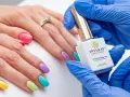 Kolorowy manicure hybrydowy krok po kroku. Dłoń z paznokciami w pastelowych barwach, kosmetyczka trzyma buteleczkę lakieru.