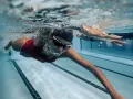 Une femme en maillot de bain rouge nage en crawl, lunettes de natation sur le nez. Sa **natation transformation physique femme** est visible sous l'eau.