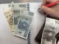 Zapisywanie wydatków na dziecko z orzeczeniem o potrzebie kształcenia specjalnego. Na zeszycie leżą banknoty 200, 100, 50 i 10 zł.