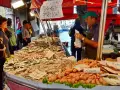 Mercato Venezia: bancarella di pesce fresco con gamberi, calamari e pesciolini. Venditore con cappellino verde.