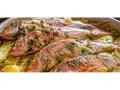 Cuatro salmonetes al horno, dorados y con hierbas, reposan sobre patatas laminadas en una fuente blanca.