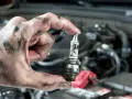 A mechanic's greasy hand holds a used spark plug, a reminder that many cars still have spark plugs for ignition.
