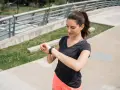 Kobieta w sportowym stroju sprawdza na zegarku tętno 180 po intensywnym treningu na zewnątrz.