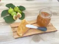 Fetta di pane con marmellata di fichi, accanto a un vasetto e a fichi freschi su un tagliere di legno.