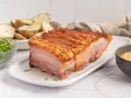 Panceta de cerdo al horno con piel crujiente, acompañada de patatas asadas y ensalada.