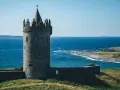 Kamienny zamek w Irlandii, z charakterystyczną wieżą i blankami, góruje nad błękitnym morzem.