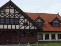 Elewacja budynku w stylu mur pruski, z charakterystyczną drewnianą szachownicą na jasnym tle i ceglanym parterem.
