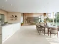 Ampio open space con cucina moderna, isola in marmo e zona pranzo. Pavimenti diversi creano continuità visiva tra gli ambienti.