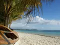 Mauritius pora deszczowa. Drewniana łódź na piaszczystej plaży pod palmami, turkusowe morze i błękitne niebo z chmurami.