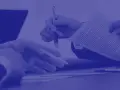 Dwie dłonie trzymają dokument, jedna z długopisem, druga wskazuje na tekst. To forma dokumentowa.