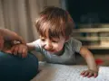 Małe dziecko z rudymi włosami, z zapłakaną buzią, trzyma się ręki dorosłego.