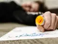 Dłoń trzymająca otwartą butelkę z lekami, obok rozsypane tabletki na kartce z napisem "Rx".
