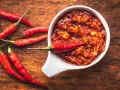 Scharfes Essen stillen: Eine Schale mit feuriger Chilisauce und frischen roten Chilis auf einem Holztisch.