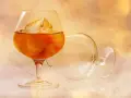 Kieliszek z bursztynowym płynem i lodem, obok pusty, przewrócony kieliszek. Idealny sposób, jak pić brandy.