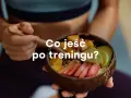 Miseczka z owocami i napisem "Co jeść po treningu?". Zdrowy posiłek regeneracyjny.