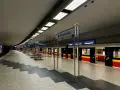 Pusta platforma stacji metra M1 Politechnika z pociągiem i tablicami kierunkowymi do Kabat i Młocin.