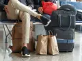 Osoby czekają na lotnisku z bagażem. Widać plecak, torby podróżne i papierowe torby na zakupy. To typowy nouvelair bagaż.