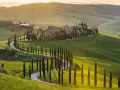Un suggestivo itinerario Val d'Orcia 3 giorni: cipressi fiancheggiano una strada tortuosa tra dolci colline verdi al tramonto.