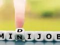 Würfel zeigen "MINIJOB". Ein Finger dreht den Würfel mit "D" zu "N", um "MINIJOB" zu bilden. Ideal für flexible Stunden pro Woche.