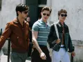 Tre uomini camminano insieme, uno con giacca marrone, uno con polo a righe e uno con giacca di jeans. Un look uomo di stile.