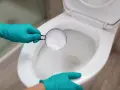 Hands in teal gloves pour baking soda into a toilet bowl, a method for how to unclog toilet without plunger.