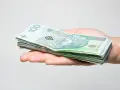 Stos banknotów 100 zł na dłoni, symbolizujący środki do zgłoszenia spadku do urzędu skarbowego.