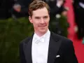 Benedict Cumberbatch w czarnym smokingu i eleganckim białym krawacie, z uśmiechem pozuje na czerwonym dywanie.