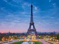 Torre Eiffel iluminada al atardecer, uno de los iconos franceses más reconocidos, con el cielo azul y nubes rosadas.