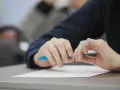 Uczeń pisze wypracowanie, przygotowując się do matury 2026. Na biurku biała kartka i niebieski długopis. Lektury obowiązkowe czekają.