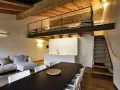 Modern living space with a loft bedroom accessible by stairs. The **soppalco soffitto basso** features a metal railing and a stone wall.