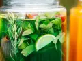Zielony, orzeźwiający syrop z mięty z dodatkiem limonki i rozmarynu w szklanym słoju. Obok pomarańczowy napój.