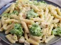 Penne z kurczakiem i kremowym sosem, obficie posypane zielonymi różyczkami brokułów. Pyszne makaron z brokułami na talerzu.